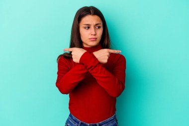 Mavi arka plan noktalarında izole edilmiş genç Hintli kadın iki seçenek arasında seçim yapmaya çalışıyor..