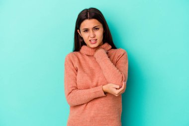 Genç Hintli bir kadın mavi arka planda izole edilmiş, dirsek masajı yapıyor, kötü bir hareketin ardından acı çekiyor..