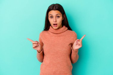 Mavi arka planda izole edilmiş genç Hintli kadın farklı kopya alanlarını gösteriyor, birini seçiyor, parmaklarıyla gösteriyor..