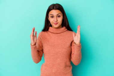 Genç Hintli kadın mavi arka planda izole edilmiş. Elinde küçük bir işaret parmağı olan, gülümseyen ve kendinden emin bir şey tutuyor..