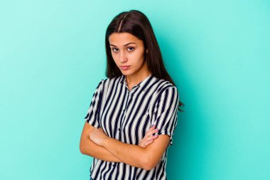 Mavi arka planda izole edilmiş genç Hintli kadın hoşnutsuzca kaşlarını çatmış, kollarını kavuşturmuş..