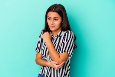 Mavi arka planda izole edilmiş genç Hintli kadın kafası karışmış, şüpheli ve güvensiz hissediyor..