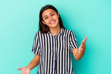 Mavi arka planda izole edilmiş genç Hintli kadın hoş bir ifade sergiliyor..