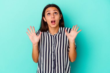 Genç Hintli kadın mavi arka planda izole edilmiş, gökyüzüne haykırıyor, yukarı bakıyor, hayal kırıklığına uğramış..