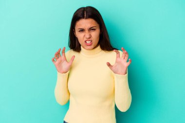 Mavi arka planda izole edilmiş genç Hintli kadın pençelerini kedi taklidi yaparken gösteriyor, agresif bir hareket..