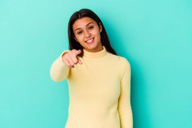 Mavi arka planda izole edilmiş genç Hintli kadın parmaklarıyla ön tarafı işaret ediyor..