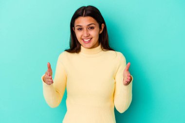 Mavi arka planda izole edilmiş genç Hintli kadın iki eliyle bir şey tutuyor, ürün sunumu..