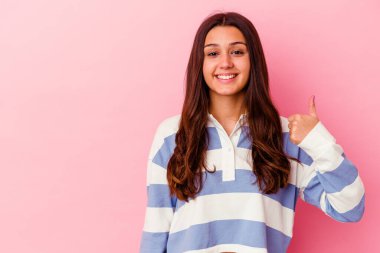 Pembe arka planda izole edilmiş genç Hintli kadın gülümsüyor ve başparmağını kaldırıyor.