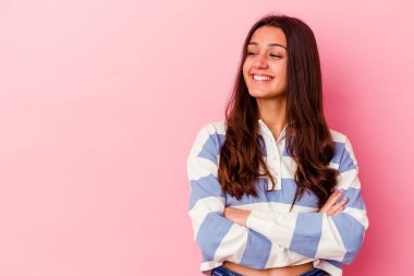 Pembe arka planda izole edilmiş genç Hintli kadın kollarını kavuşturarak gülümsüyor..