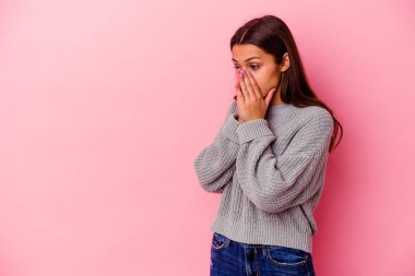 Genç Hintli bir kadın pembe arka planda izole edilmiş. Düşünceli bir şekilde fotokopi odasına bakıyor. Ağzını eliyle kapatıyor..