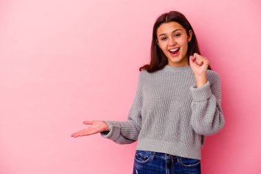 Pembe arka planda izole edilmiş genç Hintli kadın avuç içinde fotokopi alanı tutuyor, el üstünde tutuyor. Şaşırmış ve mutlu..