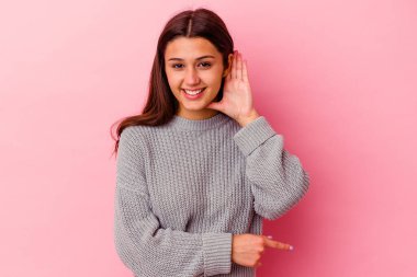 Pembe arka planda izole edilmiş genç Hintli kadın bir dedikoduyu dinlemeye çalışıyor..