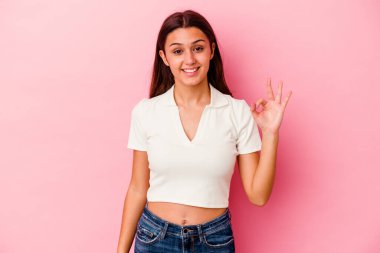 Pembe arka planda izole edilmiş genç Hintli kadın bir göz kırptı ve elleriyle iyi bir jest yaptı..