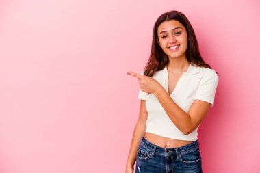 Pembe arka planda izole edilmiş genç Hintli kadın gülümsüyor ve boş alanda bir şeyler gösteriyor..