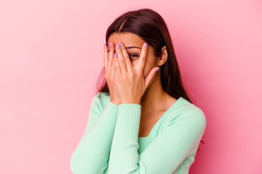 Pembe arka planda izole edilmiş genç Hintli kadın kameraya parmaklarıyla göz kırpıyor, yüzünü kapatmaktan utanıyor..