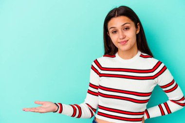 Mavi arka planda izole edilmiş genç Hintli kadın bir avuç içinde fotokopi alanı ve belinde bir el daha olduğunu gösteriyor..