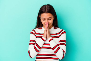 Mavi arka planda izole edilmiş genç Hintli bir kadın el ele tutuşup dua ederken kendine güveniyor..