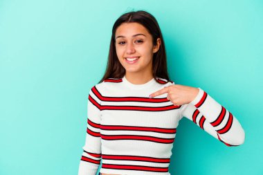 Mavi arka planda yaşayan genç Hintli bir kadın gömleğin fotokopi odasını elle işaret ediyor, gururlu ve kendinden emin.