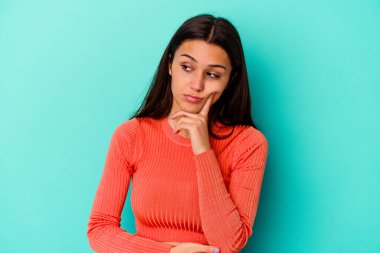 Genç Hintli bir kadın mavi arka planda izole edilmiş. Bir strateji planlıyor, bir iş yolu düşünüyor..