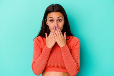 Mavi arka planda izole edilmiş genç bir Hintli kadın şok olmuş, elleriyle ağzını kapatmış, yeni bir şey keşfetmek için sabırsızlanıyor..