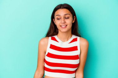Mavi arka planda soyutlanmış genç bir Hintli kadın gülümsüyor, neşeli ve keyifli görünüyor..