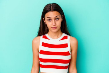 Genç Hintli bir kadın mavi arka planda izole edilmiş üzgün, ciddi bir yüz, mutsuz ve hoşnutsuz.