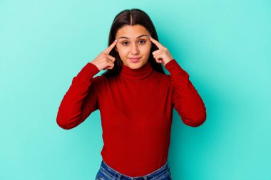 Mavi arka planda izole edilmiş genç Hintli kadın bir göreve odaklanmış, işaret parmaklarını işaret ediyor..