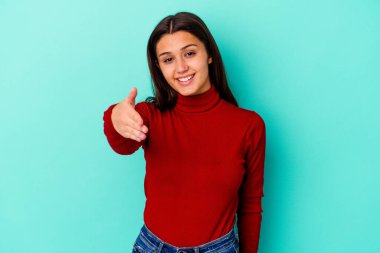 Mavi arka planda izole edilmiş genç Hintli kadın selamlaşma jesti olarak kameraya elini uzatıyor..