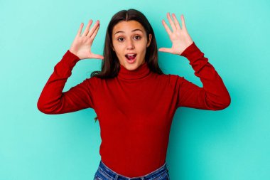 Genç Hintli kadın mavi arka planda zaferi ya da başarıyı kutlarken şaşırdı ve şok oldu..