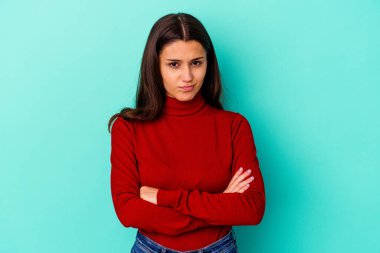 Mavi arka planda izole edilmiş genç Hintli kadın yanakları patlatıyor, yorgun bir ifadesi var. Yüz ifadesi kavramı.