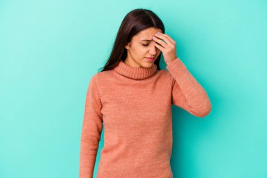 Genç Hintli bir kadın mavi arka planda izole edilmiş, başı ağrıyor, yüzüne dokunuyor..