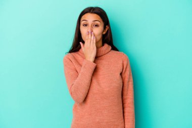 Mavi arka planda izole edilmiş genç bir Hintli kadın şok olmuş, elleriyle ağzını kapatmış, yeni bir şey keşfetmek için sabırsızlanıyor..