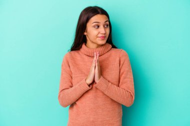 Genç Hintli kadın mavi arka planda izole edilmiş dua ediyor, bağlılık gösteriyor, dindar biri ilahi ilham arıyor..