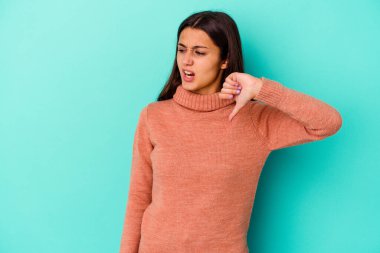 Mavi arka planda izole edilmiş genç Hintli kadın baş parmağını aşağı gösteriyor ve hoşlanmadığını ifade ediyor..