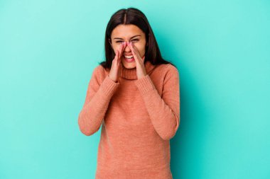 Genç Hintli bir kadın mavi arka planda izole edilmiş bir şekilde dedikodu yapıyor, bir şeyleri haber veriyor..