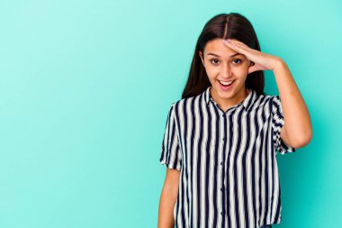 Mavi arka planda izole edilmiş genç Hintli kadın yüksek sesle bağırıyor, gözlerini açık ve ellerini gergin tutuyor..