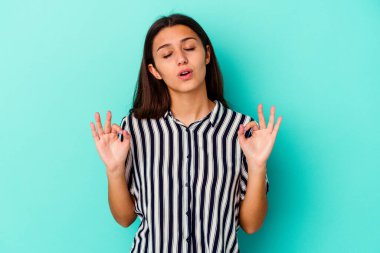 Mavi arka planda izole edilmiş genç Hintli kadın yoğun bir günün ardından rahatlıyor, yoga yapıyor..