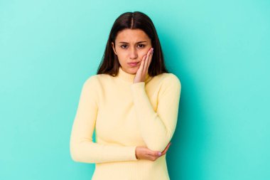 Mavi arka planda izole edilmiş genç Hintli kadın yanakları patlatıyor, yorgun bir ifadesi var. Yüz ifadesi kavramı.