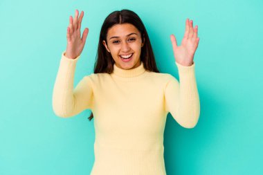 Genç Hintli kadın mavi arka planda zaferi ya da başarıyı kutlarken şaşırdı ve şok oldu..