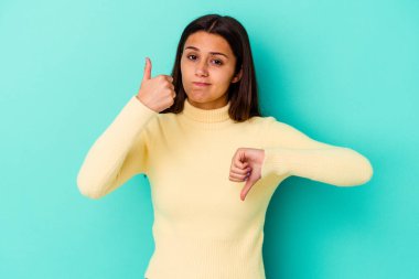 Mavi arka planda izole edilmiş genç Hintli kadın baş parmağını kaldırıyor, zor seçim konsepti.
