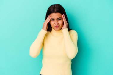Genç Hintli bir kadın mavi arka planda izole edilmiş, başı ağrıyor, yüzüne dokunuyor..