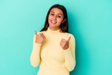 Genç Hintli kadın mavi arka planda izole edilmiş. Baş parmağını kaldırıyor, gülümsüyor ve kendinden emin..