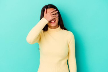 Mavi arka planda soyutlanmış genç bir Hintli kadın elleriyle gözlerini kapatıyor, geniş bir gülümsemeyle bir sürpriz bekliyor..