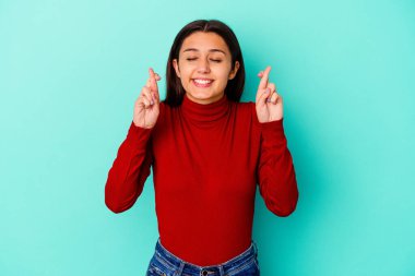 Genç Hintli kadın mavi arka planda izole edilmiş şans dilemek için şans diliyor.