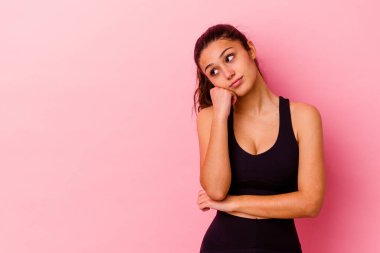 Genç Hintli kadın pembe arka planda izole edilmiş üzgün ve dalgın hisseden, kopyalama alanına bakan.