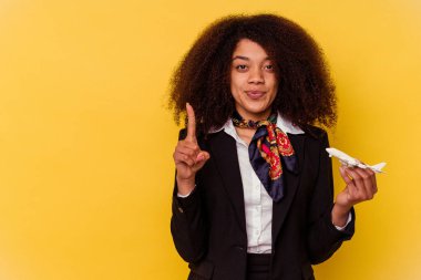 Genç Afrikalı Amerikalı hostes sarı arka planda izole edilmiş küçük bir uçak tutuyor..
