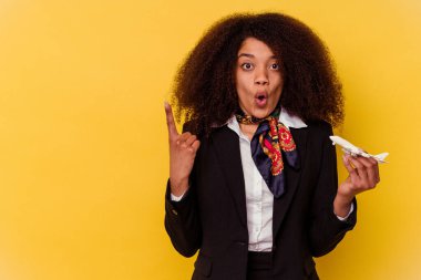 Genç Afrikalı Amerikalı hostes sarı arka planda izole edilmiş küçük bir uçak tutuyor.