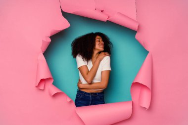 Kırık kağıda sarılmış genç Afrikalı Amerikalı kadın mavi arka plan kucaklamalarında yalnız, kaygısız ve mutlu..