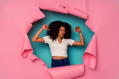 Mavi arka planda izole edilmiş yırtık kağıda sarılı genç Afrikalı Amerikalı kadın gururlu ve kendinden emin hissediyor, örnek olarak..