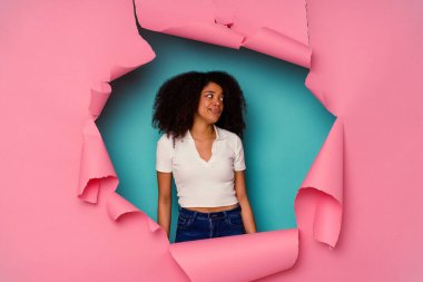 Kırık kağıda sarılı genç Afrikalı Amerikalı kadın mavi arka planda izole edilmiş kafası karışmış, şüpheci ve emin değil.